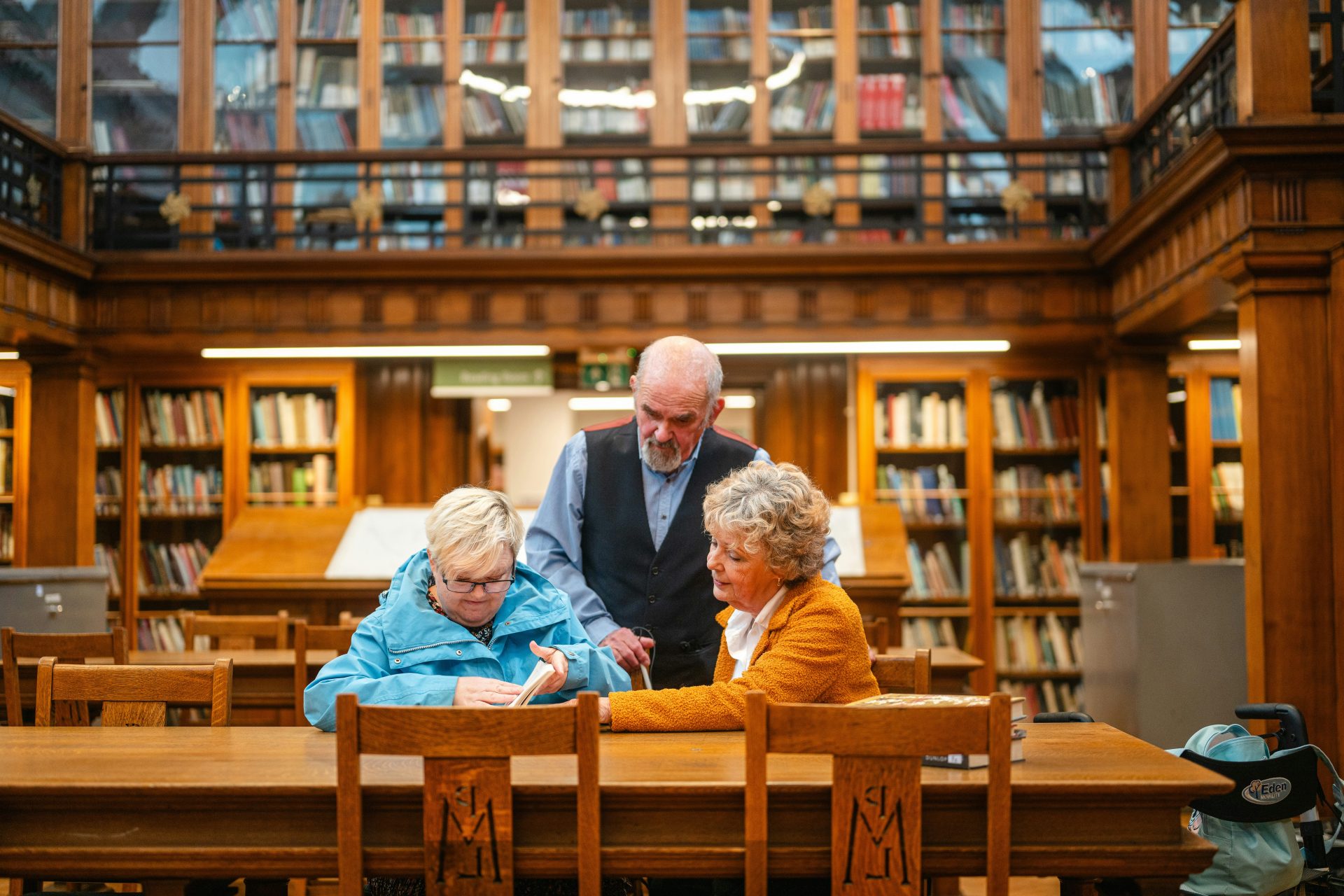 Three people gathered at a wooden table in library.